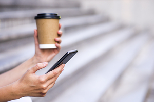 Close up of a businesswoman using mobile phone and holding paper cup. Close-up detail of a businesswoman hand holding paper cup and using a smartphone